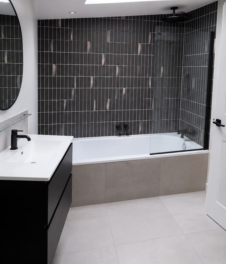 The same bathroom after refurbishment by Platinum Handy Services: dark feature tiling, a black vanity unit, round mirror and new bath.