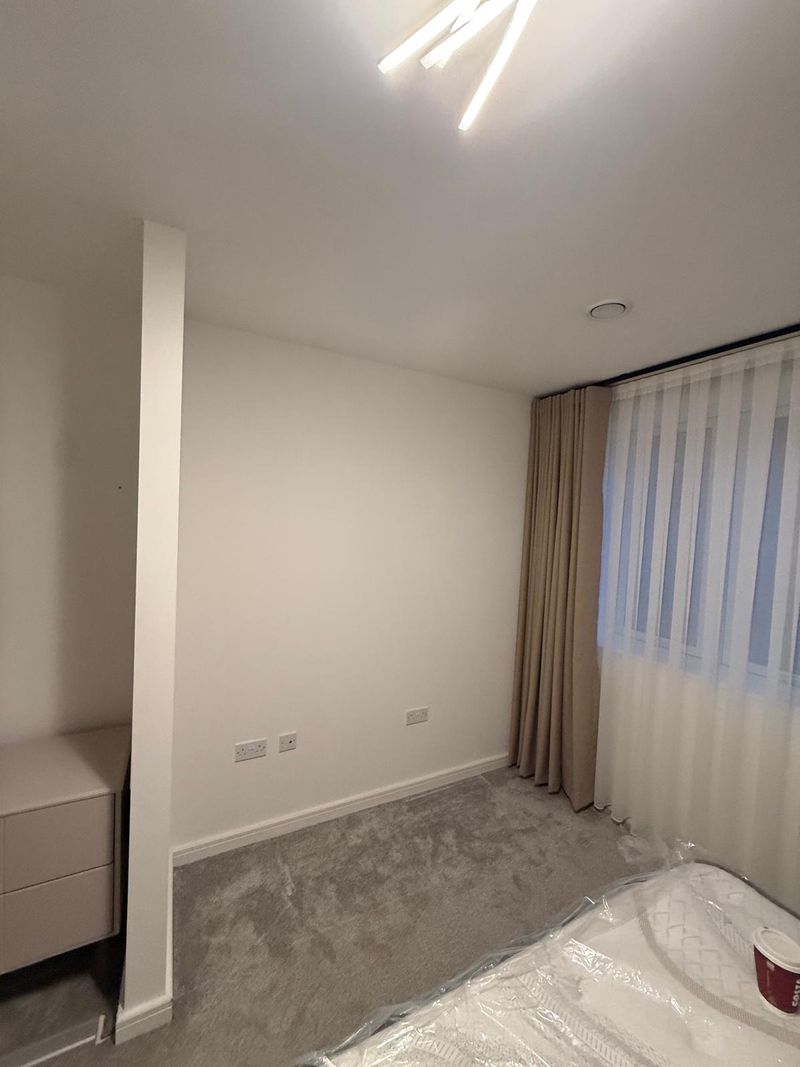 A freshly decorated bedroom with new grey carpet, painted walls and floor-length curtains with voiles, fitted by Platinum Handy Services.