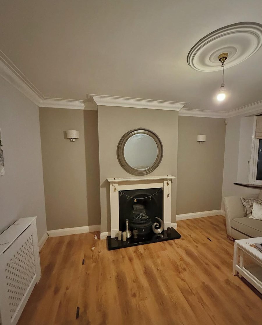 A freshly decorated living room with painted walls, new coving, a ceiling rose and wood-effect flooring, refurbished by Platinum Handy Services.