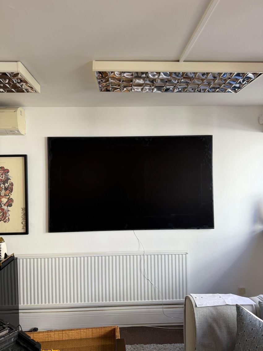 A large flat-screen television wall-mounted level on a white wall by Platinum Handy Services, with the tool case below.